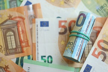 Roll of twenty euro currency bills lies on big amount of hundred and fifty euro banknotes
