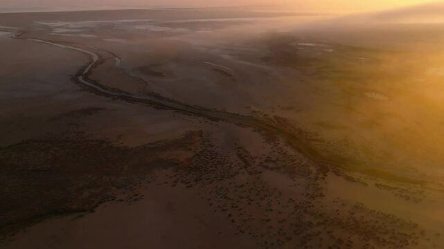 Cinematic drone side movement over a river in the desert sands on the shore of Lake Tuz in misty sunrise