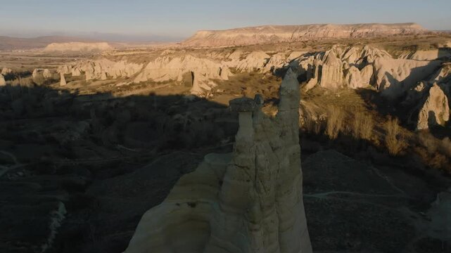 Drone flight between elongated unusual rock formations resembling chimneys or phalluses, illuminated by the sunset at the Love Valley in Cappadocia