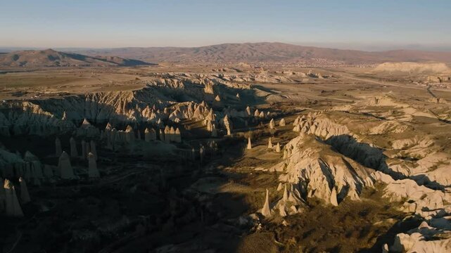 Drone view from above at sunset of the elongated rocks in the Love Valley resembling chimneys or phalluses, with mountains in the background in Cappadocia