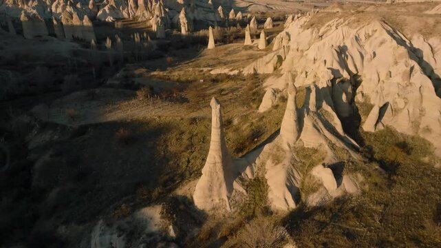 Drone flight between elongated unusual rock formations resembling chimneys or phalluses, illuminated by the sunset at the Love Valley in Cappadocia