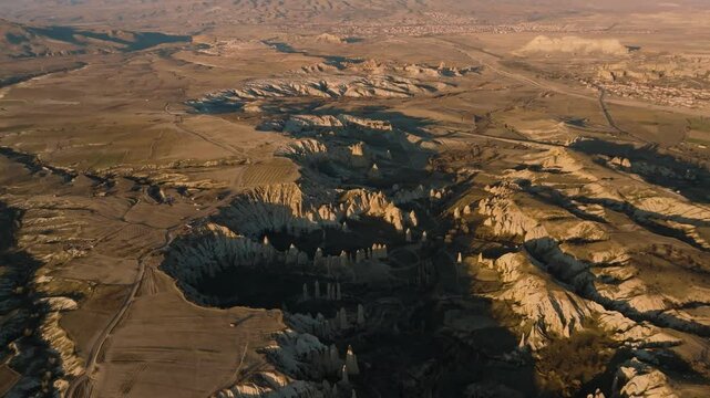 Drone view from above at sunset of the elongated rocks in the Love Valley resembling chimneys or phalluses, with mountains in the background in Cappadocia