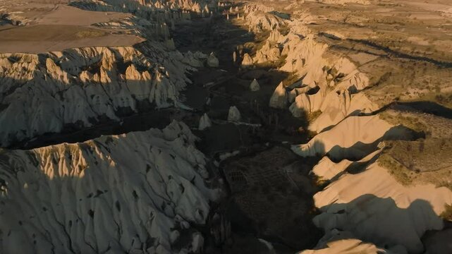Drone view from above at sunset of the elongated rocks in the Love Valley resembling chimneys or phalluses, with mountains in the background in Cappadocia