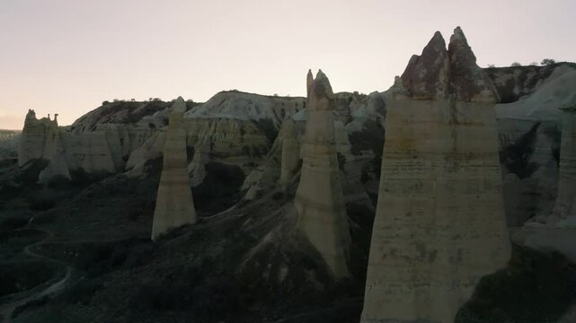Drone flight between elongated unusual rock formations resembling chimneys or phalluses, illuminated by the sunset at the Love Valley in Cappadocia