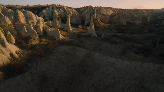 Drone flight between elongated unusual rock formations resembling chimneys or phalluses, illuminated by the sunset at the Love Valley in Cappadocia
