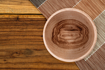 Wooden bowl with natural grain on a rustic wooden table and a textured napkin. Ideal for eco-friendly dining, food styling, and natural decor.