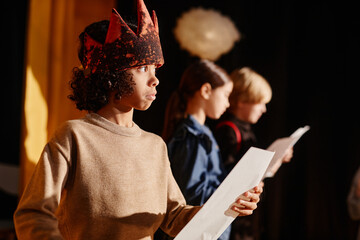 Portrait of young child engaging in school play by wearing medieval costume and holding white prop,...