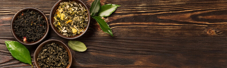 Fototapeta premium This banner showcases an assortment of tea leaves in wooden bowls on a dark wooden background. The vibrant colors and textures of the dried tea leaves are highlighted by the rustic setting