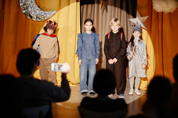 Group of children performing school play on stage with spotlight on each performer and decorations...