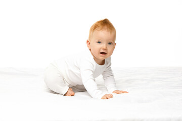 Portrait of adorable child, toddler in onesie crawling on bed, learning new, exploring surroundings against white studio background. Concept of childhood, motherhood, health. Copy space for ad