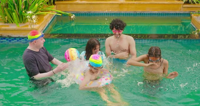 Indian wet family teen age child group standing in pool playing splash water have fun joy spend day time water park happy father dad young adult girl kid boy wear ring enjoy hotel trip resort picnic