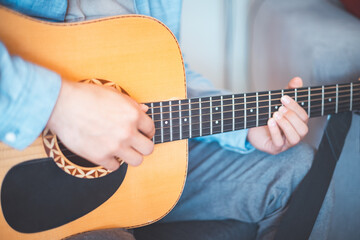 Close-up on musician strums an acoustic guitar in a cozy home, immersed in music. His casual style,...