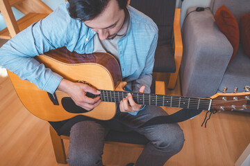 Close-up on musician strums an acoustic guitar in a cozy home, immersed in music. His casual style,...