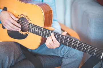 Close-up on musician strums an acoustic guitar in a cozy home, immersed in music. His casual style,...