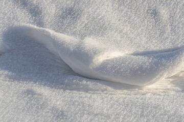 A fun small snowdrift of white snow with yellow sunshine and bokeh light at sunset on a blurred background in a park in winter