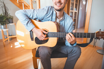 Obraz premium Man alone in the middle of a sunlit room enjoys playing a beautiful wooden acoustic guitar and composing new songs. Immersed in the sweet tones of the guitar. Music that heals the soul