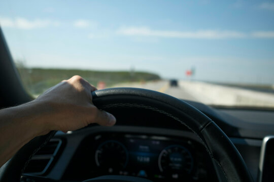 Hand on steering wheel driving on an open highway with clear blue sky in view, Everglades, Florida, USA