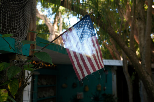 An American flag hangs in a lush, tree-filled outdoor setting, with sunlight filtering through, Florida Keys, USA