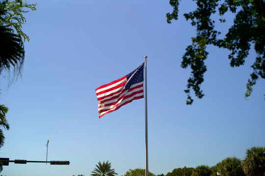 American flag waving on a tall flagpole against a clear blue sky with trees surrounding, Miami, FLorida, USA