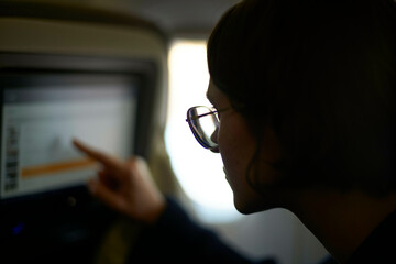 Woman wearing glasses interacting with a touchscreen on a plane.