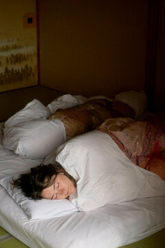 Woman sleeping comfortably on a futon bed in a dimly lit Japanese-style room, Japanese Alps, Shiba Onsen