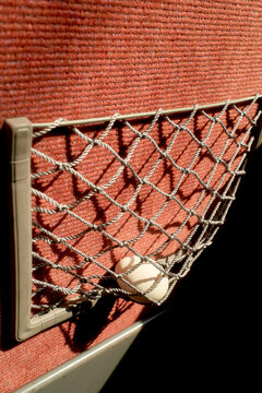 A small net pocket on a red fabric surface of a seat in a Japanese train holds a single white egg in sunlight, near Kanazawa, Japan