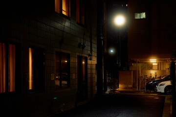 Dimly lit urban alleyway with glowing streetlights and warmly lit windows at night. Tokyo, Japan