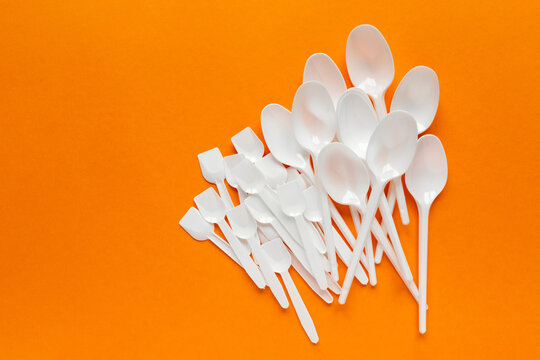 white plastic disposable cutlery on orange bachground (tablespoons, teaspoons)
environmental problem 