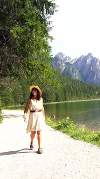 Tourist holding her straw hat admiring the stunning landscape of lake dobbiaco and the dolomites mountains in summer, italy
