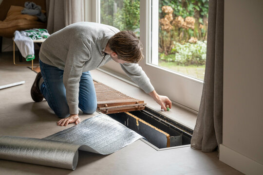 Man adjusting isolation and heating system in a modern living room beside large windows. Netherlands