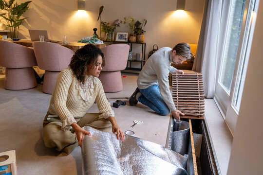 Couple installing insulation near a large window in a cozy living room setting. Netherlands