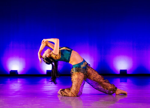 Dancer in colorful costume performs on stage with vibrant blue and purple lighting. The Nutcracker, Bainbridge Island, USA