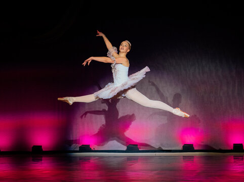 Ballet dancer in mid-air leap on stage with dramatic lighting and pink background. The Nutcracker, Bainbridge Island, USA