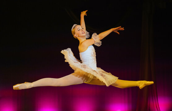 Ballerina in white tutu leaping gracefully on stage against a vibrant pink backdrop. The Nutcracker, Bainbridge Island, USA
