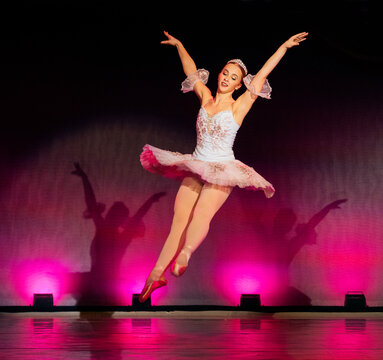 A ballerina in a pink tutu leaps gracefully on stage with vibrant lighting. The Nutcracker, Bainbridge Island, USA