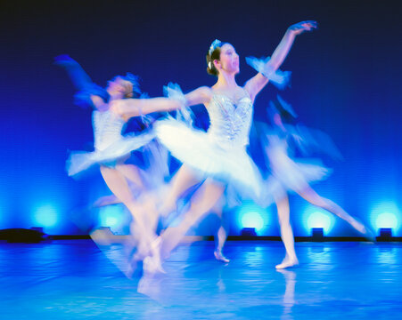 Ballet dancers in white tutus perform gracefully on a stage with blue lighting. The Nutcracker, Bainbridge Island, USA