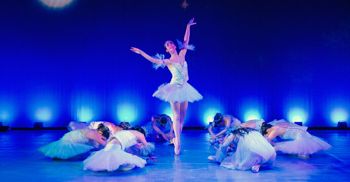 Ballerina performing center stage with dancers gracefully posed around her in a blue-lit theater. The Nutcracker, Bainbridge Island, USA