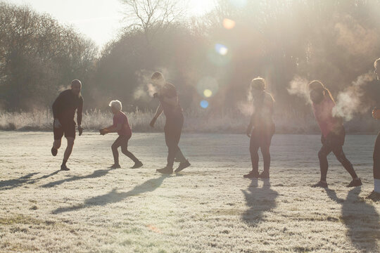 A group of people playfully run across a frosty field on a sunny morning, with their breath visible in the cold air. Sale Water Park, Manchester, UK
