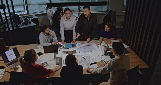 Diverse business team collaborating on project plans in a modern office. Discussing blueprints and strategies in a productive meeting.