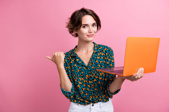 Portrait of positive cheerful woman wear print blouse hold laptop indicating at discount empty space isolated on pink color background