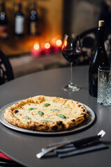 Four Cheese Pizza with a creamy sauce, featuring mozzarella, gorgonzola, parmesan, brie, and fontina, topped with fresh basil. Vertical composition with bokeh of candlelit background, and wine glass 