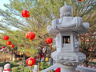 Red Chinese lanterns and a traditional stone lantern create a festive and culturally rich scene under the trees