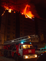 Nighttime fire truck in action near a blazing building, showcasing emergency response during an...
