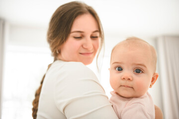 Cute small baby girl in bed at home. Woman holding little infant child.