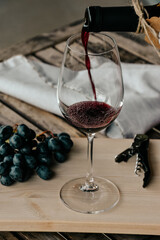 Pouring red wine into glass on a rustic table with a bunch of red grapes