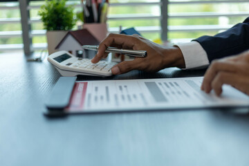 Naklejka premium A man is sitting at a desk with a calculator and a piece of paper with numbers on it. He is pointing to the paper and he is explaining something to someone. The scene suggests a professional setting 