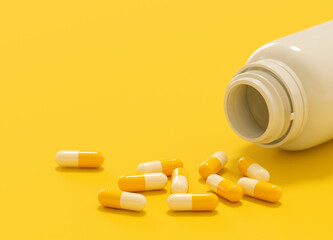 Some yellow and white capsules poured out of a plastic bottle on yellow background with copy space.