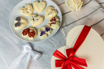 Heart-shaped white chocolate platter with flowers and gift box on marble surface