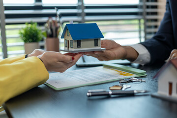 A man and a woman are holding a blue house model and a key. The woman is wearing a yellow jacket
