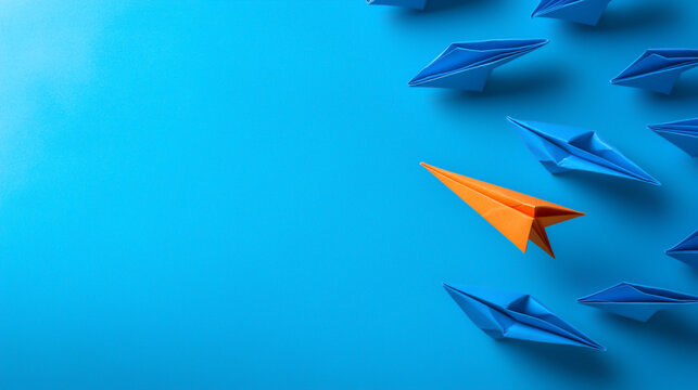 An orange paper plane leads a cluster of blue paper planes on a blue background.